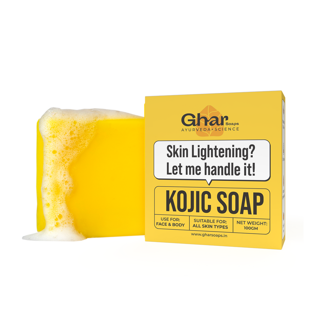 A yellow bar of soap with bubbles is placed next to a yellow box labeled “KOJIC SOAP” for skin lightening by Ghar, suitable for all skin types, 100g.